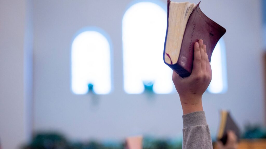 man hand holding bible up during worship service