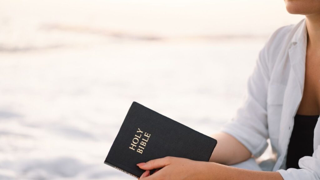Christian woman holds bible in her hands. Reading the Holy Bible on the sea during beautiful sunset. Concept for faith, spirituality and religion. Peace, hope