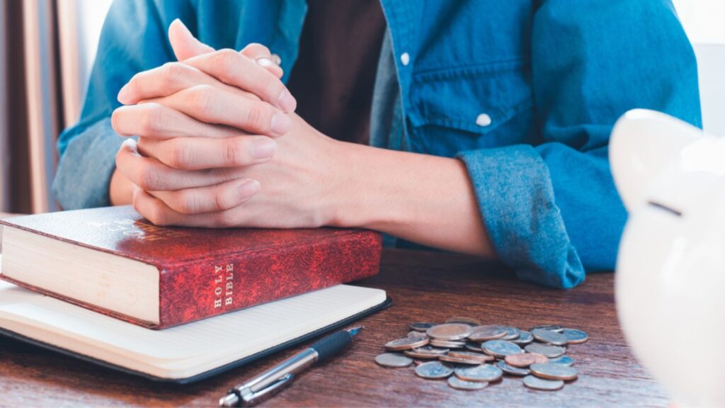 Man praying near Bible next to a pile of coins