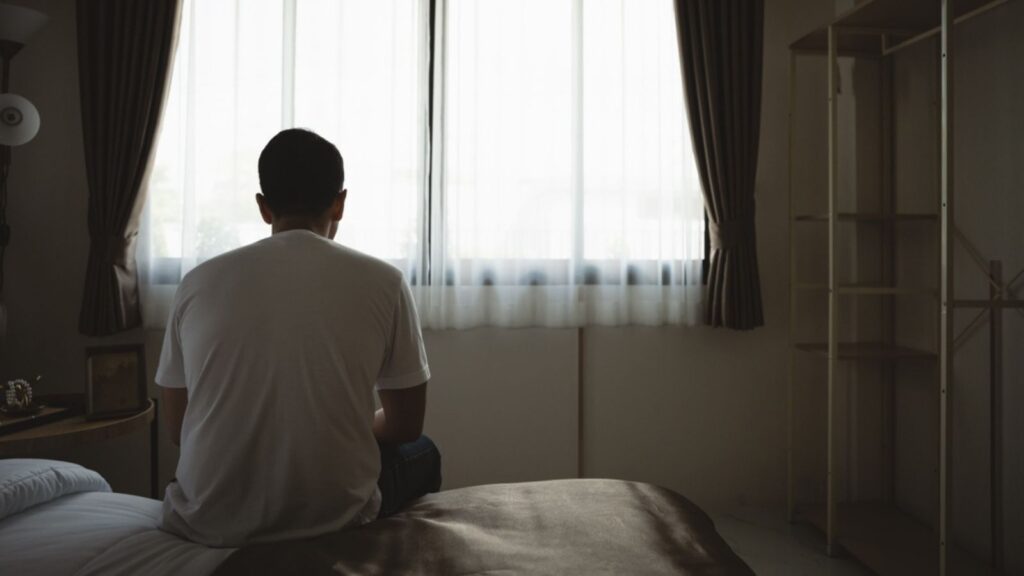 Silhouette depressed man sadly sitting on the bed in the bedroom. Sad man suffering depression insomnia awake and sit alone on the bed in bedroom. Depression health people concept.