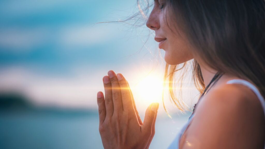 Young woman meditating with her eyes closed, practicing Yoga with hands in prayer position