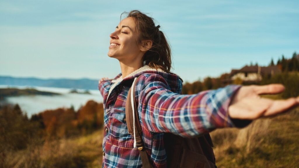 overjoyed woman backpacker wearing a checkered jacket opening arms into the sky. girl enjoying the view on mountain hills