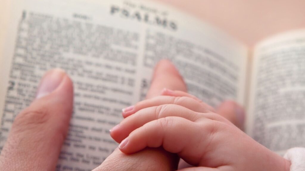 Baby holding father's finger as he points to Psalms verse