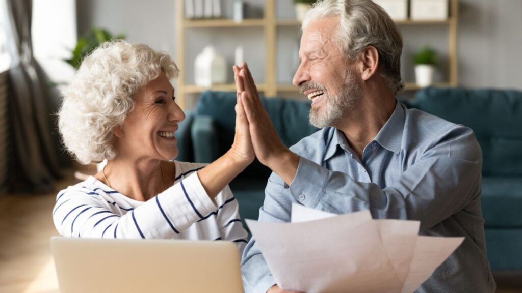 Excited senior couple giving high five, mature family celebrating success, checking or paying domestic bills