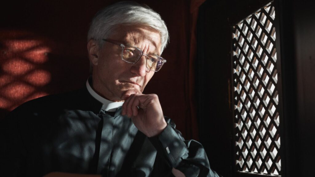 Senior priest sitting behind the grid and listening the confession in the church