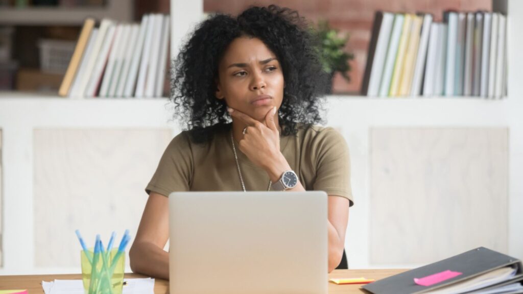 Thoughtful concerned woman worker student feeling uncertain bored doubtful solving problem at work with laptop, puzzled black