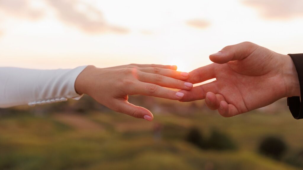 hand of man and woman reaching and touching to each other with love on nature sunset sky background. Valentines day. Concept of human relation, community, togetherness, teamwork, love, symbolism